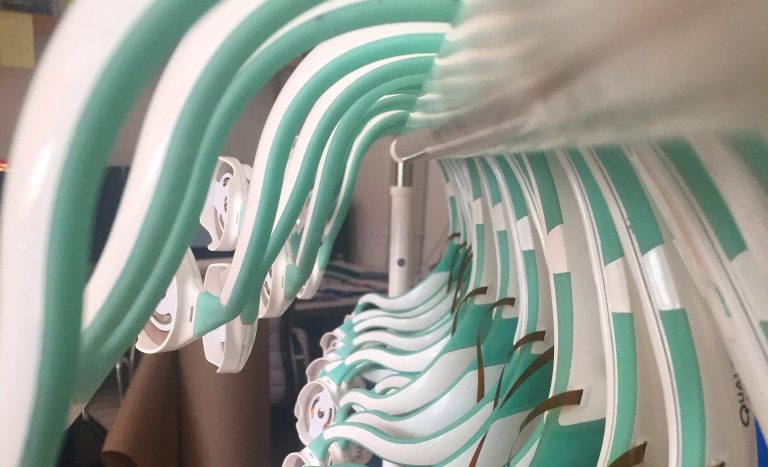 Row of identical curved plastic device housings with integrated flex circuits staged on a rack—illustrating DFM focus on repeatability, alignment, and scalable assembly